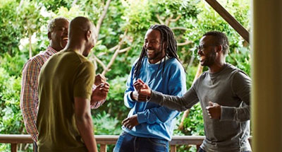 Image of four black men laughing while hanging out on a porch with trees in the background.